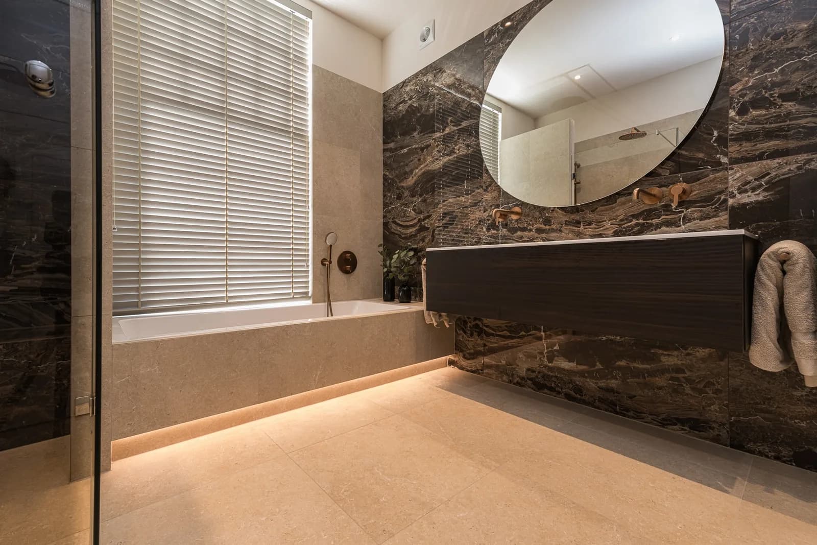 Ruime wellness badkamer in Wageningen met marmerlook wand en rond spiegel