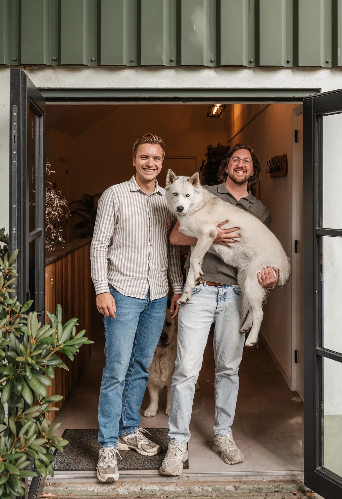 Pascal van de Braak tilt hond Bodi op in de deuropening van het kantoor, Gerwin Morren lacht