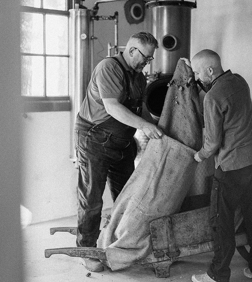 Twee makers van Kegel Spirits vullen een ketel in de stokerij, in zwart-wit